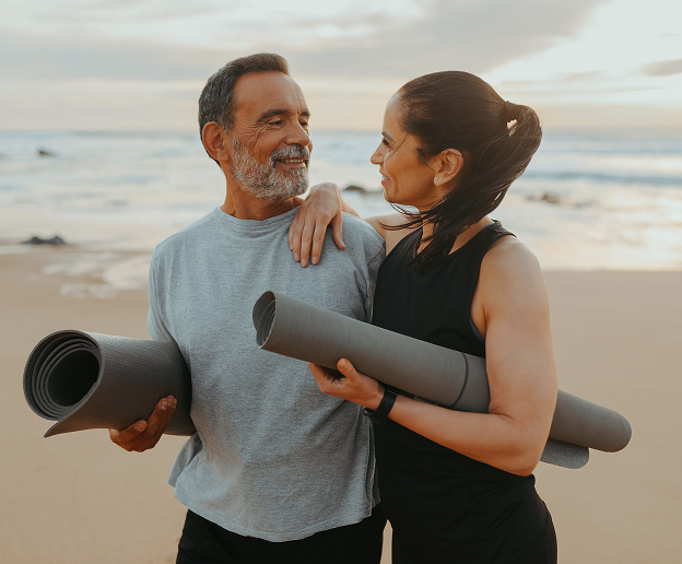 Couple smiling on the beach with yoga mats